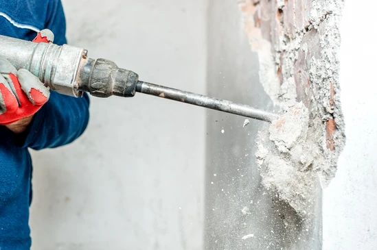 Ouvrier en combinaison bleue utilisant un marteau-piqueur pneumatique pour démolir un mur en béton et briques