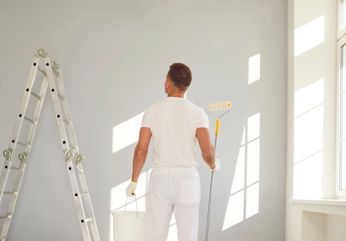 Professionnel peintre homme, se tient dans un appartement armé d'une brosse à rouleaux et seau lors d'une rénovation