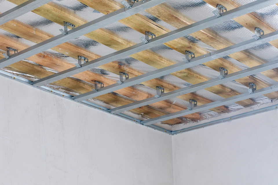 Chantier de rénovation intérieur en cours avec ouvriers installant une structure de faux plafond suspendu